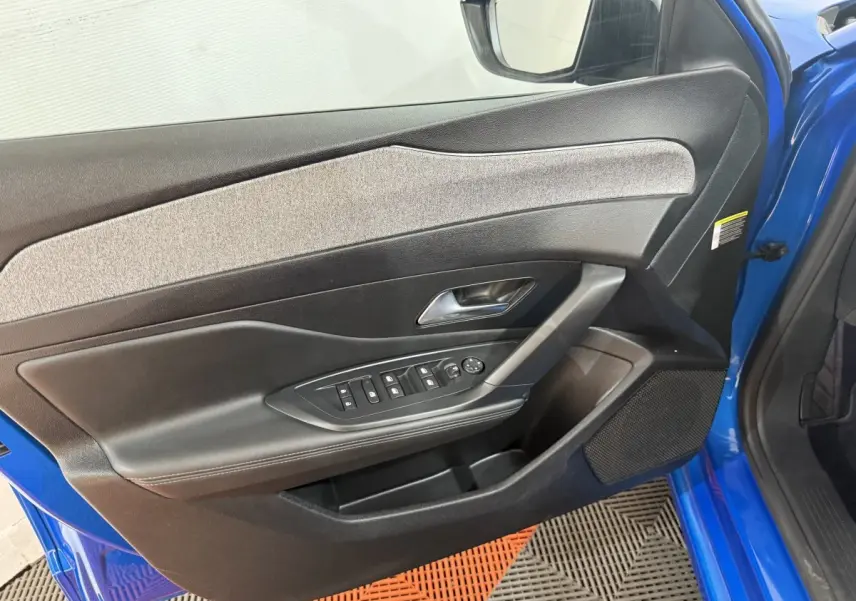 Vue rapprochée de la porte avant gauche bleu vif d'une Peugeot 308 2023 avec commandes électriques et garniture grise.