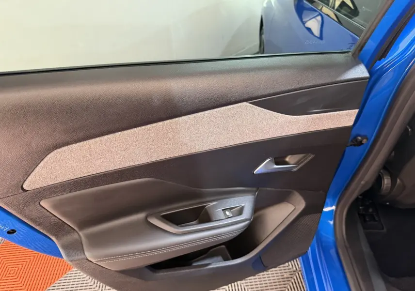 Vue intérieure de la porte avant gauche bleu vif d'une Peugeot 308 2023 avec garniture noire et beige.