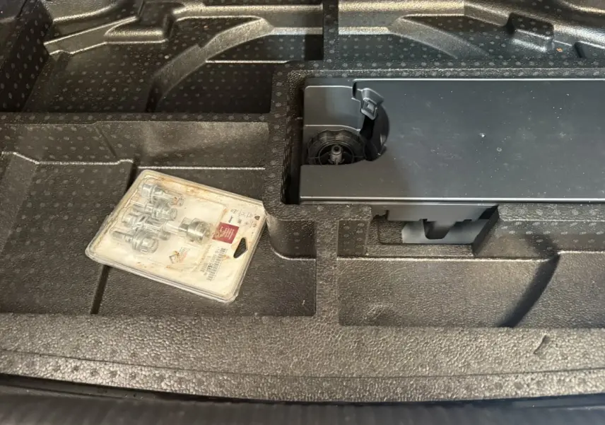Gros plan sur le rangement en mousse noire du coffre d'une Peugeot 308 bleu, avec un kit de visserie posé dessus.