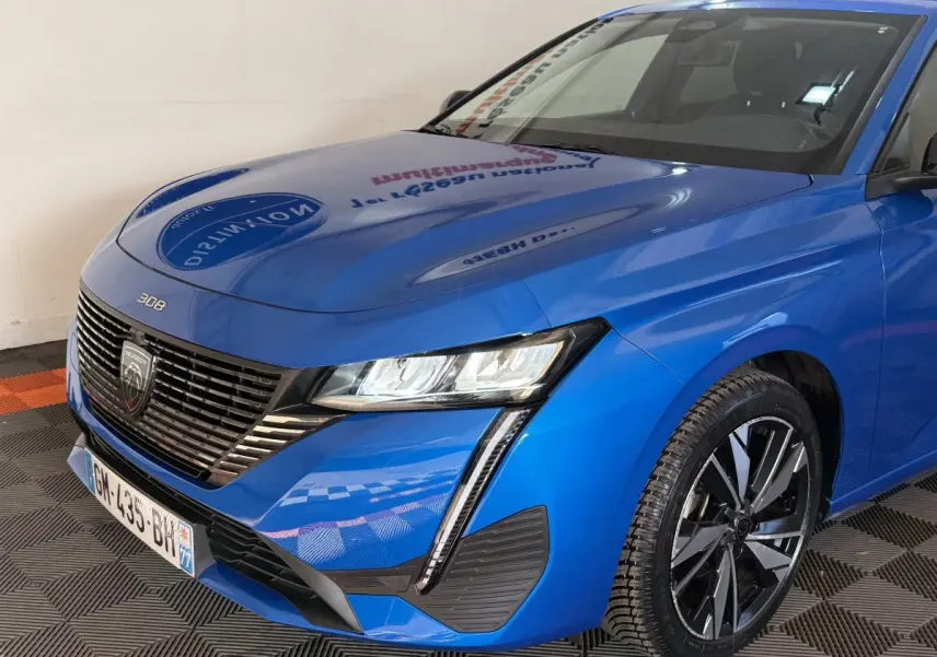 Vue 3/4 avant droit d'une Peugeot 308 bleu vif avec calandre noire et phares LED distinctifs.