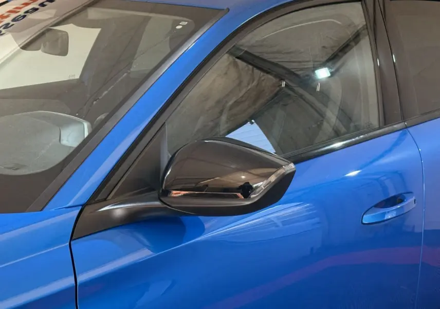 Vue rapprochée du rétroviseur côté gauche d'une Peugeot 308 bleu vif, avec poignée de porte assortie visible.