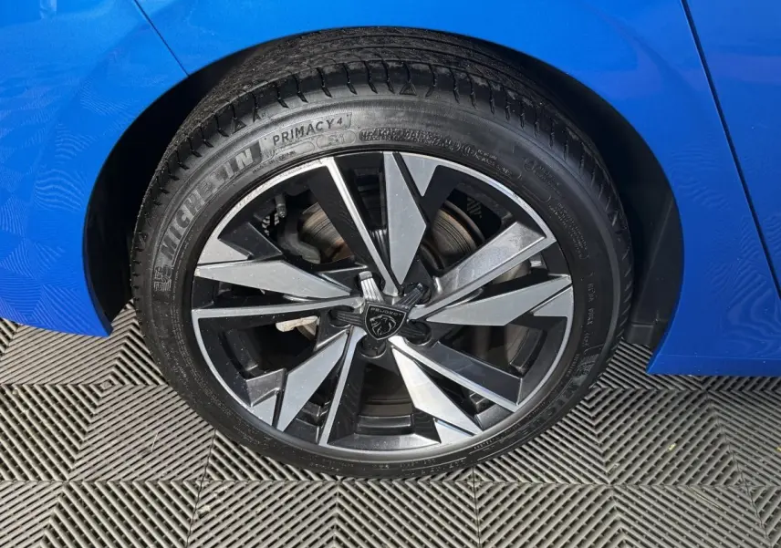 Gros plan sur la roue avant gauche d'une Peugeot 308 bleu 2023, jante alliage au design moderne et pneu Michelin.