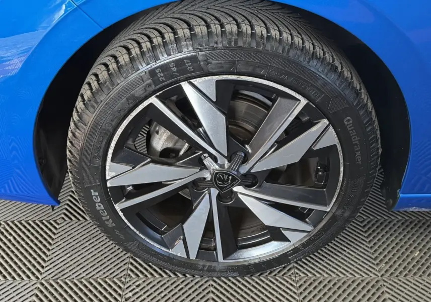 Gros plan sur la roue avant gauche d'une Peugeot 308 bleu 2023 avec jante alliage noire et argentée.