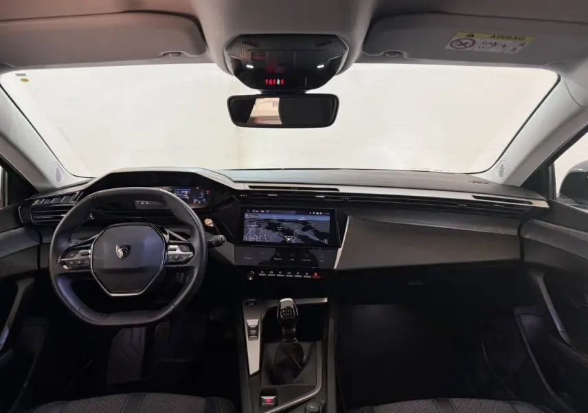 Intérieur avant de la Peugeot 308 PureTech 130 S&S Allure Pack 2023, tableau de bord noir avec écran tactile central et volant cuir.