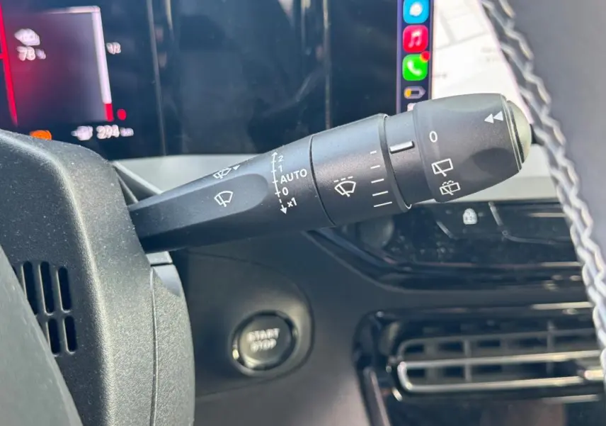 Gros plan sur la commande des essuie-glaces à gauche du volant dans l’habitacle noir de l’Opel Mokka électrique gris 2025.