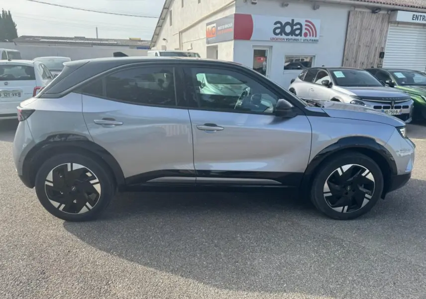 Vue de profil côté gauche d’un Opel Mokka électrique gris 2025 avec jantes alliage 17 pouces et vitres surteintées.