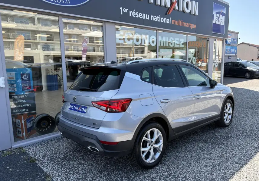 Vue 3/4 arrière droite d’un SEAT Arona 2024 gris clair métallisé, avec jantes alliage et toit noir.