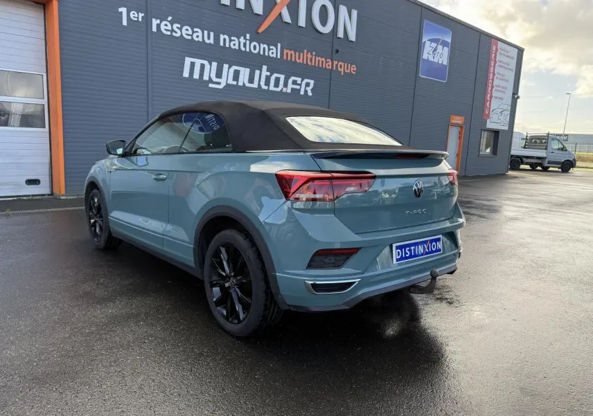 Vue 3/4 arrière droite d'un Volkswagen T-Roc Cabriolet vert cactus avec capote noire et attelage amovible.