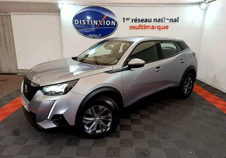 Peugeot 2008 gris clair vue 3/4 avant droit dans un showroom avec éclairage et logo Distinxion en arrière-plan