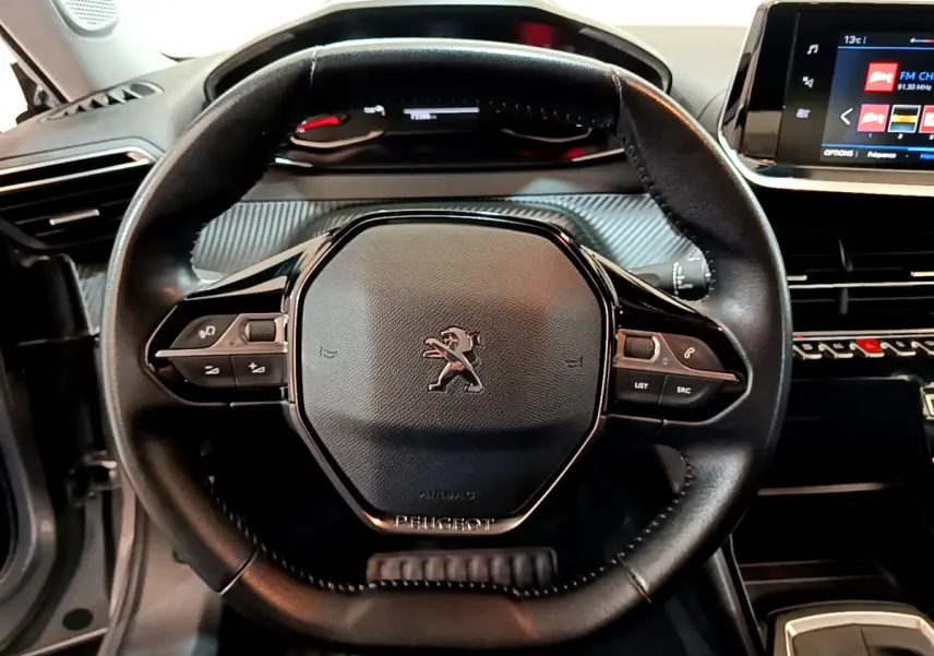 Vue rapprochée du volant cuir multifonctions noir de la Peugeot 2008, avec tableau de bord et écran tactile visibles.