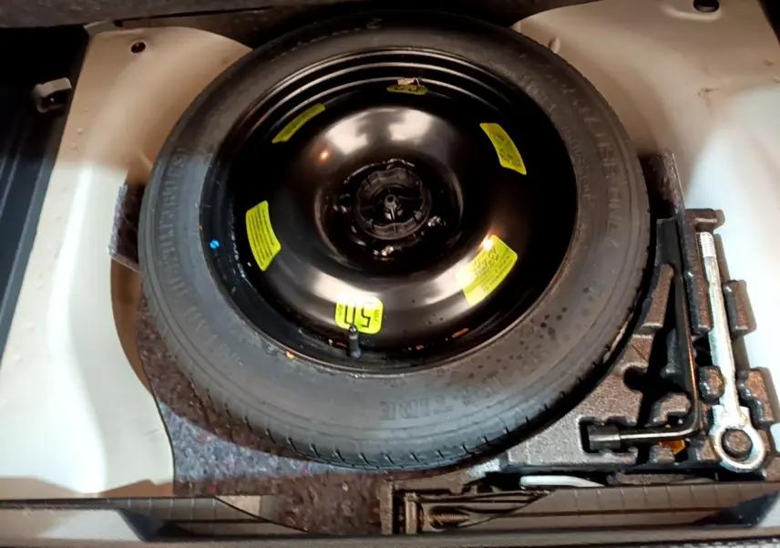 Vue plongeante sur la roue de secours noire et les outils de bord dans le coffre d'une Peugeot 2008 gris clair.