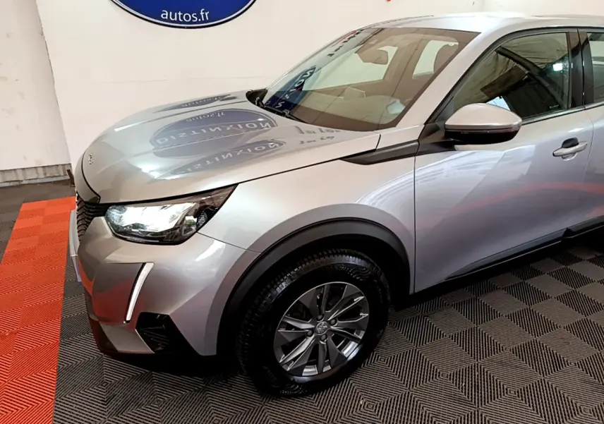 PEUGEOT 2008 gris clair en 3/4 avant gauche, avec feux LED et jantes alliage visibles sur sol intérieur.