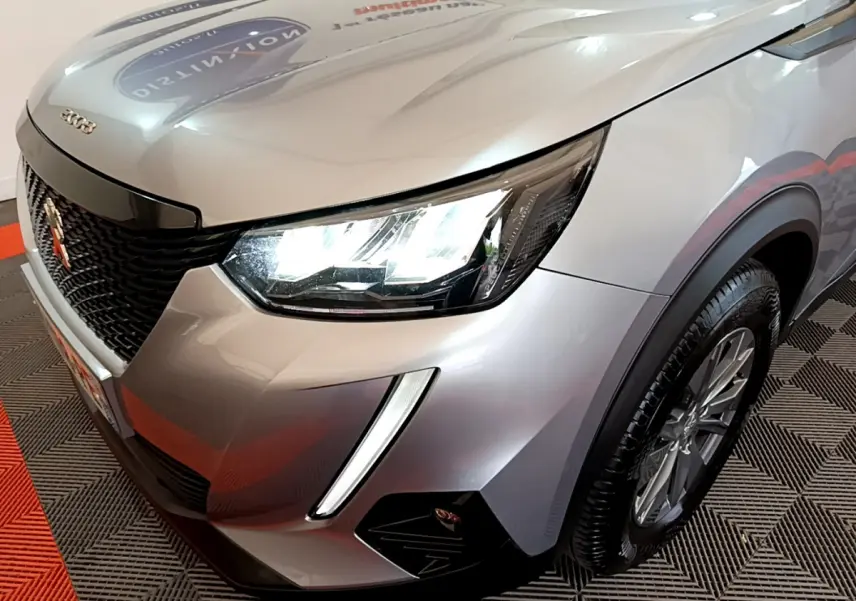 Vue 3/4 avant droit d'un Peugeot 2008 gris clair avec phares LED et calandre noire distinctive.