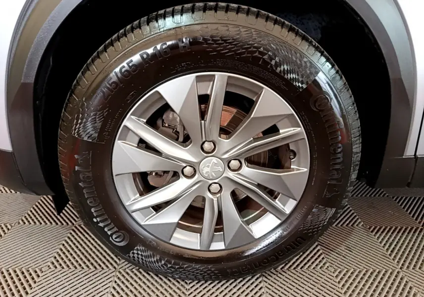 Gros plan sur la roue avant droite avec jante alliage argentée et logo Peugeot sur un Peugeot 2008 gris clair.