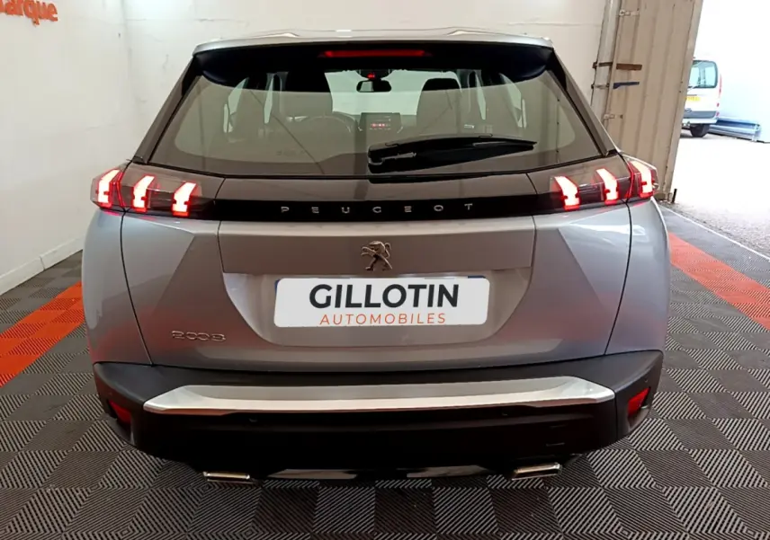 Vue arrière d'un Peugeot 2008 gris clair avec feux LED allumés dans un garage showroom.
