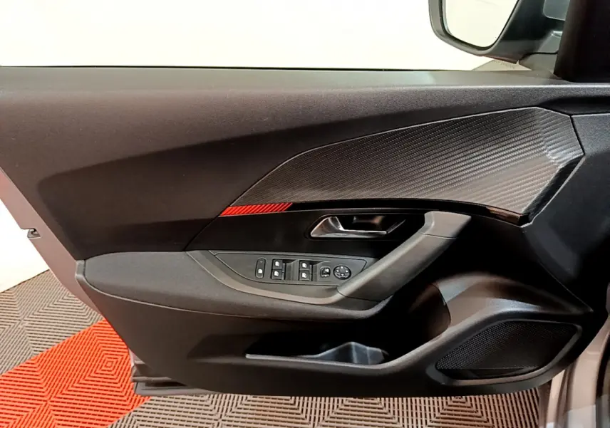Gros plan sur la porte avant gauche du Peugeot 2008 gris clair, avec commandes électriques et insert décoratif noir texturé.