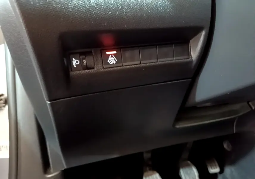 Gros plan sur les commandes de réglage des phares et désactivation de l'ESP côté gauche du tableau de bord noir du Peugeot 2008 gris clair.