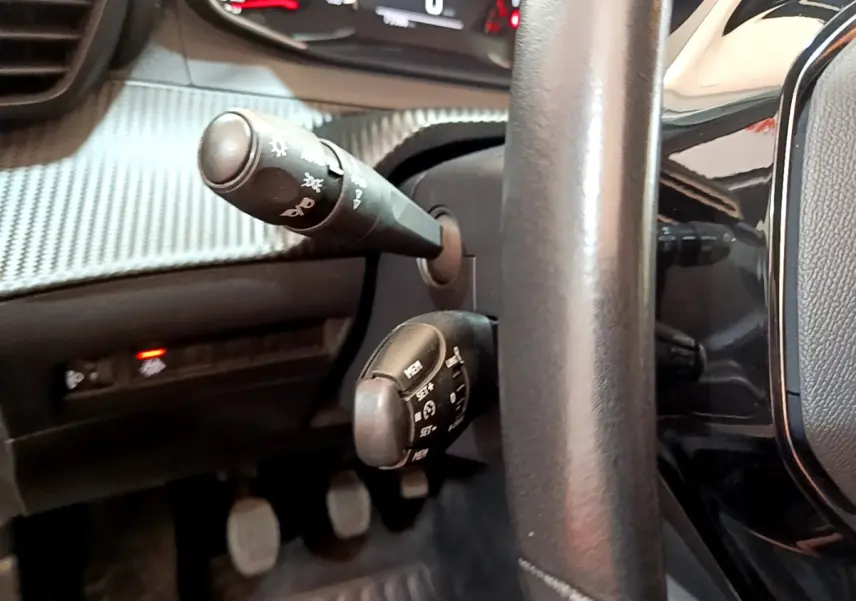 Gros plan sur les commandes au volant cuir noir d'une Peugeot 2008 2020, avec tableau de bord et pédales visibles.