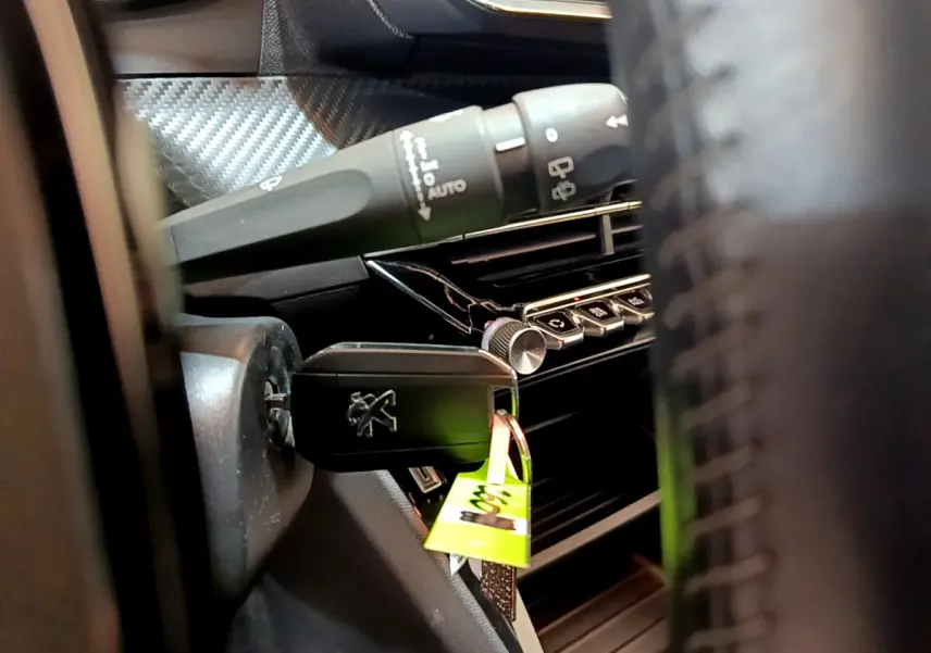 Gros plan sur la clé insérée dans le contacteur d'une Peugeot 2008 gris clair, avec commandes du tableau de bord visibles.