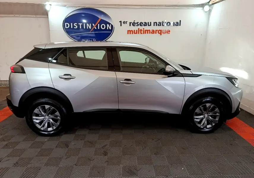 Peugeot 2008 gris clair vue de profil côté gauche, avec jantes alliage et toit noir contrasté en intérieur showroom.