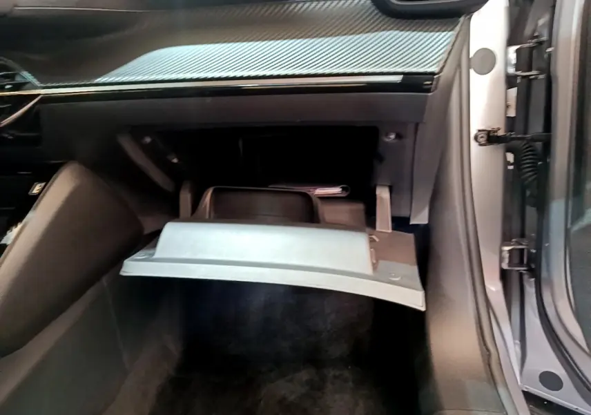 Gros plan sur la boîte à gants ouverte côté passager du Peugeot 2008 gris clair, montrant l'intérieur noir et le tableau de bord.