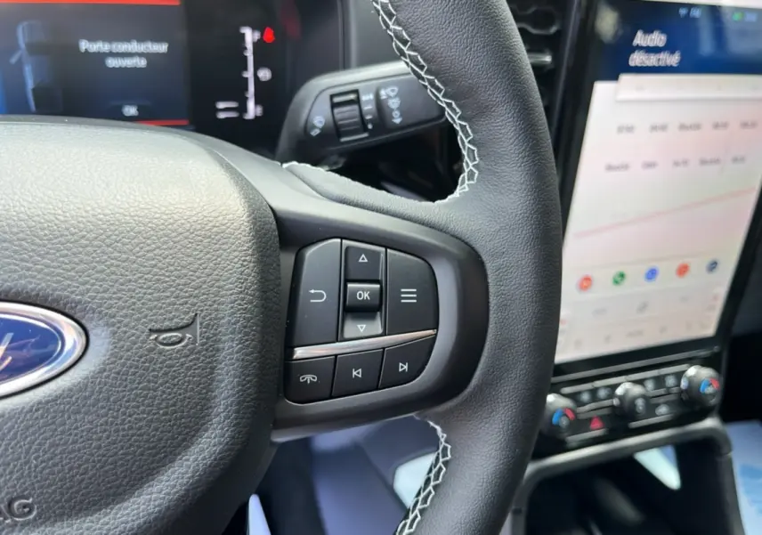 Gros plan sur le volant cuir multifonctions du Ford Ranger 2.3 PHEV 281 E-AWD, avec écran tactile et commandes au volant visibles.