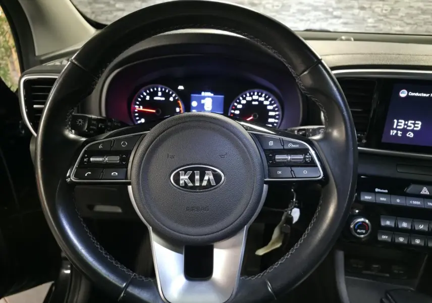 Vue rapprochée du volant cuir noir KIA avec commandes intégrées et tableau de bord éclairé du Sportage 2021.