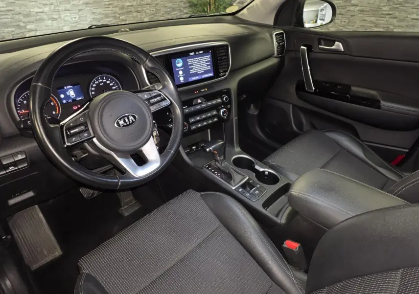 Vue intérieure côté conducteur du Kia Sportage 1.6 CRDI MHEV noir, montrant tableau de bord et console centrale avec volant cuir.
