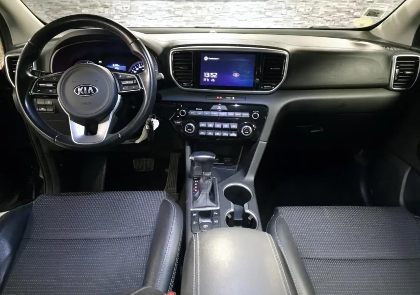 Vue intérieure avant du Kia Sportage noir, tableau de bord avec écran tactile 8 pouces et volant cuir multifonction.