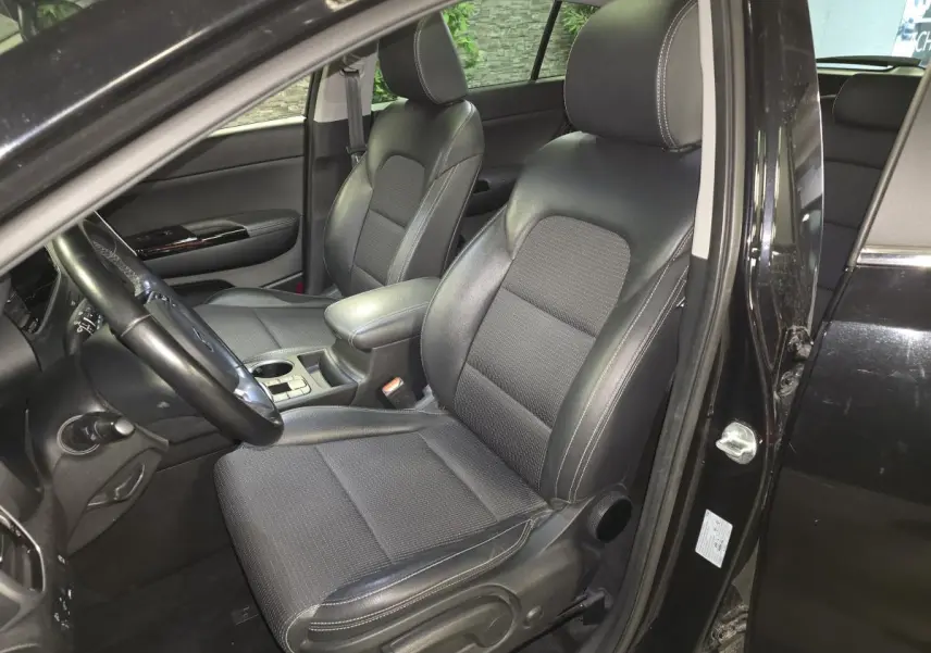Vue intérieure côté conducteur du Kia Sportage noir 2021, mettant en valeur les sièges cuir/tissu et l'accoudoir central.