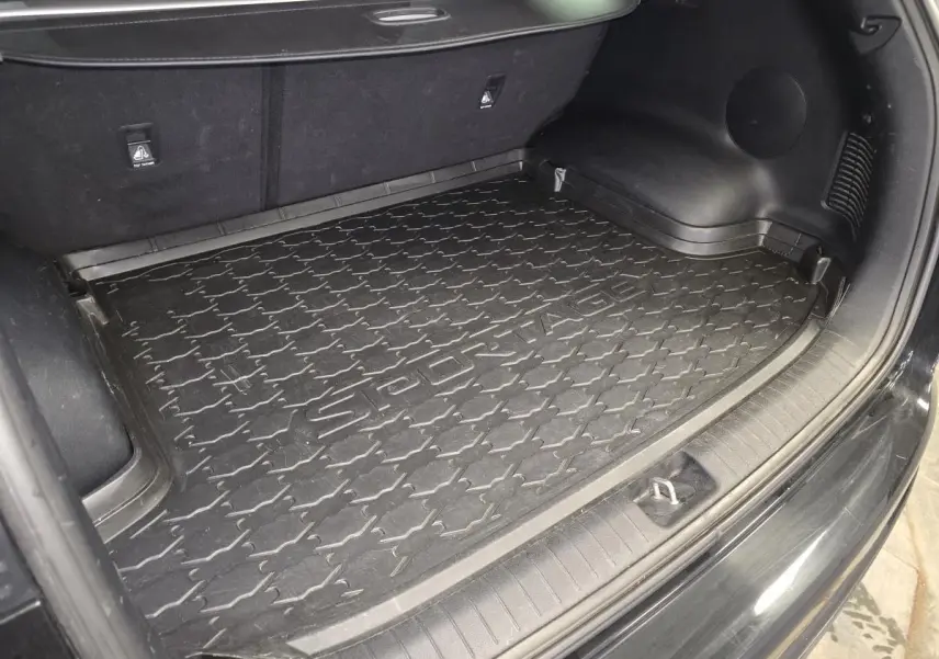 Coffre ouvert vu de l'arrière d'un KIA Sportage noir avec tapis de coffre caoutchouc marqué Sportage.