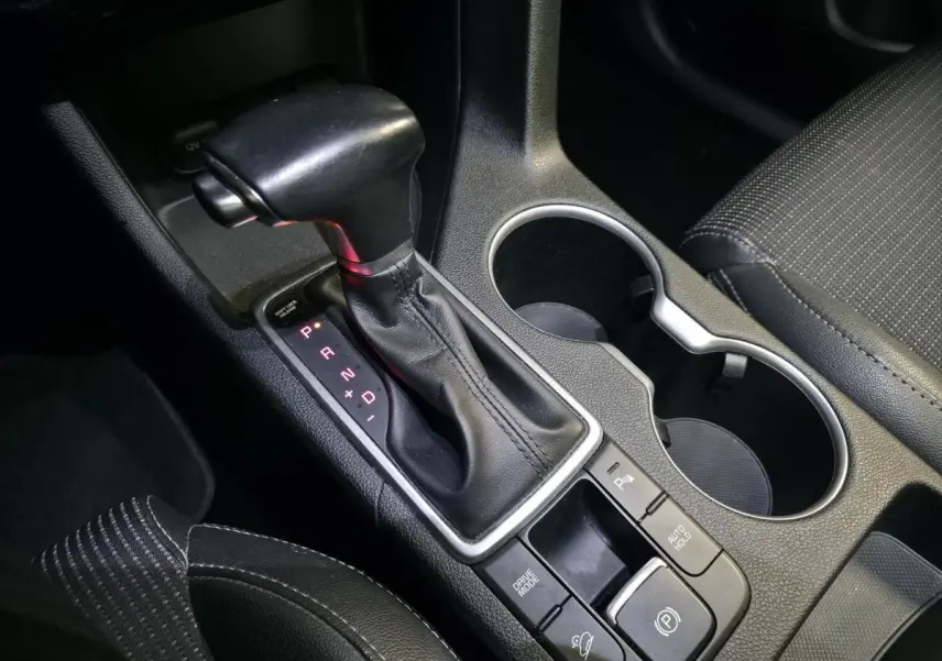 Gros plan sur la console centrale du Kia Sportage noir, mettant en valeur le levier de vitesses automatique et les porte-gobelets.