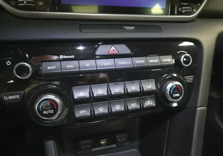 Gros plan sur la console centrale noire du Kia Sportage 1.6 CRDI MHEV avec commandes climatisation et multimédia.