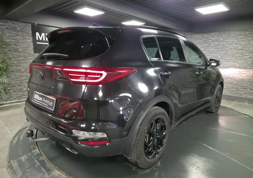 Vue 3/4 arrière droite du KIA Sportage noir Black Edition 2021 avec jantes noires et feux arrière LED allumés.