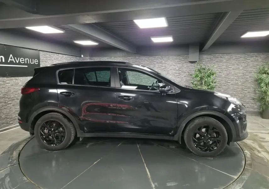 Vue de profil côté gauche d’un KIA Sportage noir 2021 avec jantes alliage noires Black Edition dans un showroom.