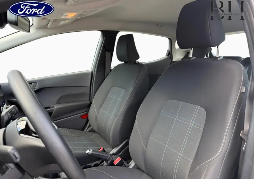 Vue intérieure avant de la Ford Fiesta 2020, sièges tissu noir à motifs, volant et portières visibles, ambiance claire.