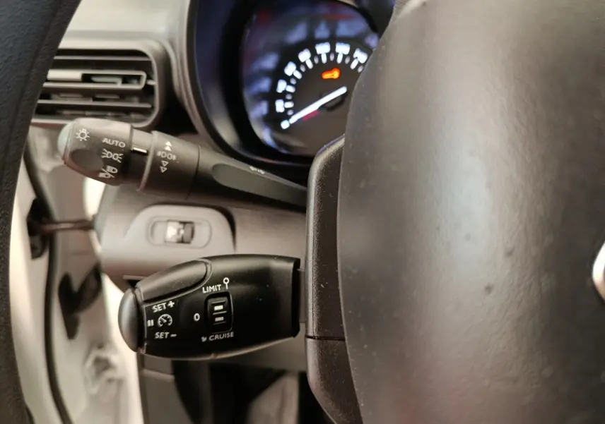 Gros plan sur le volant et commandes au volant du Citroën Berlingo blanc, affichage du compteur partiellement visible.