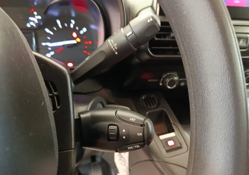 Gros plan sur la commande multifonction à gauche du volant du Citroën Berlingo blanc, tableau de bord en arrière-plan flou.