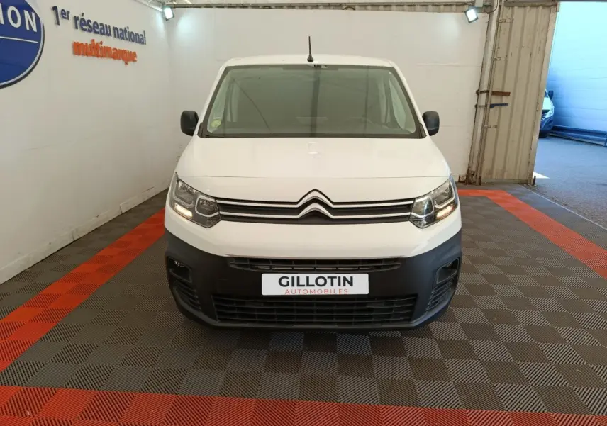Vue frontale d’un Citroën Berlingo blanc 2022 avec pare-chocs noir et phares allumés en intérieur showroom.