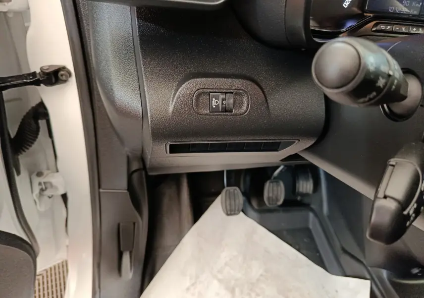 Vue intérieure côté conducteur du Citroën Berlingo blanc 2022, montrant les pédales et commandes du tableau de bord.