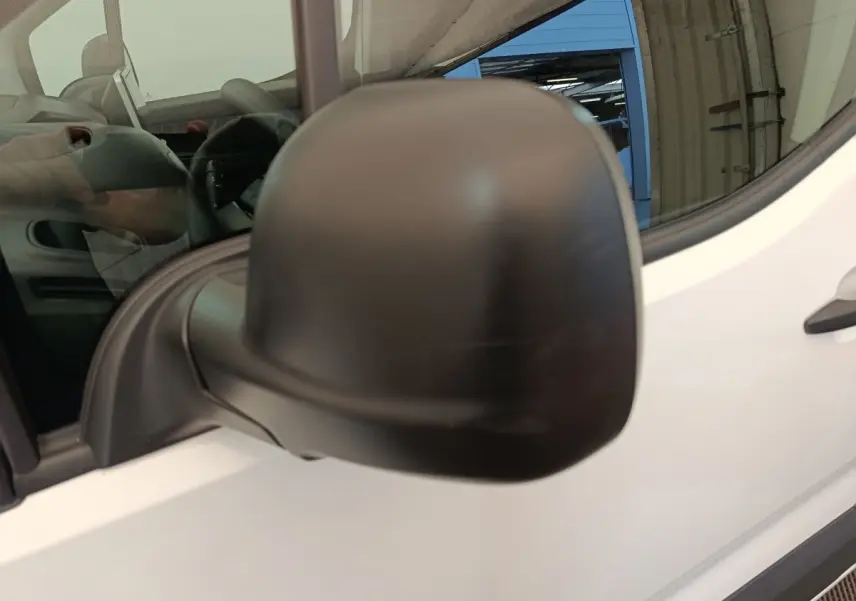 Gros plan sur le rétroviseur noir côté conducteur du Citroën Berlingo blanc, vue partielle de la porte avant.