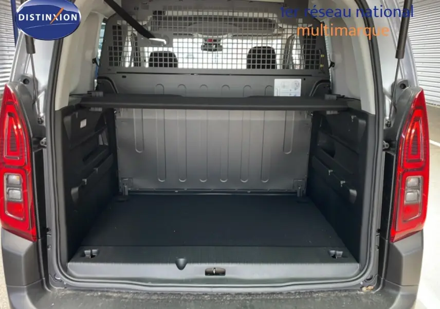 Coffre ouvert vu de l'arrière d'un Citroën Berlingo gris Artense, avec cloison métallique et espace de chargement spacieux.