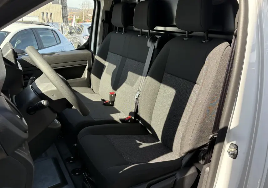 Vue intérieure côté conducteur de l'Opel Vivaro blanc 2024, montrant la banquette tissu bi-ton noir/gris et le volant réglable.