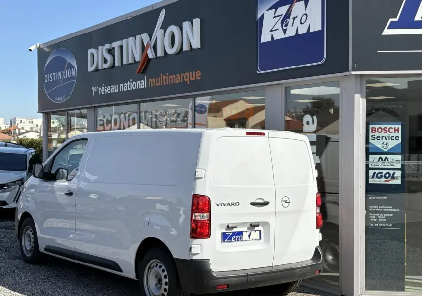 Vue 3/4 arrière droite d’un Opel Vivaro blanc 2024 stationné devant un garage multimarque.