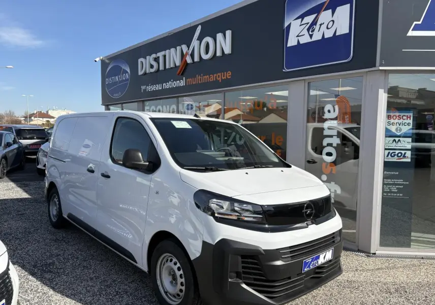 Opel Vivaro blanc en 3/4 avant droit, avec calandre noire et pare-chocs avant noir mat, stationné devant un showroom.