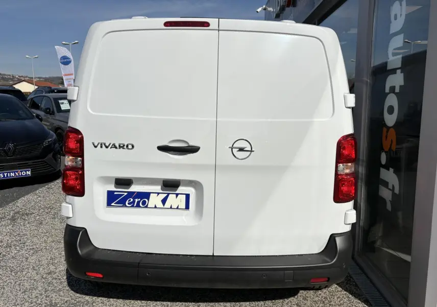 Vue arrière d’un utilitaire Opel Vivaro blanc avec portes battantes et pare-chocs noir, stationné devant un bâtiment.