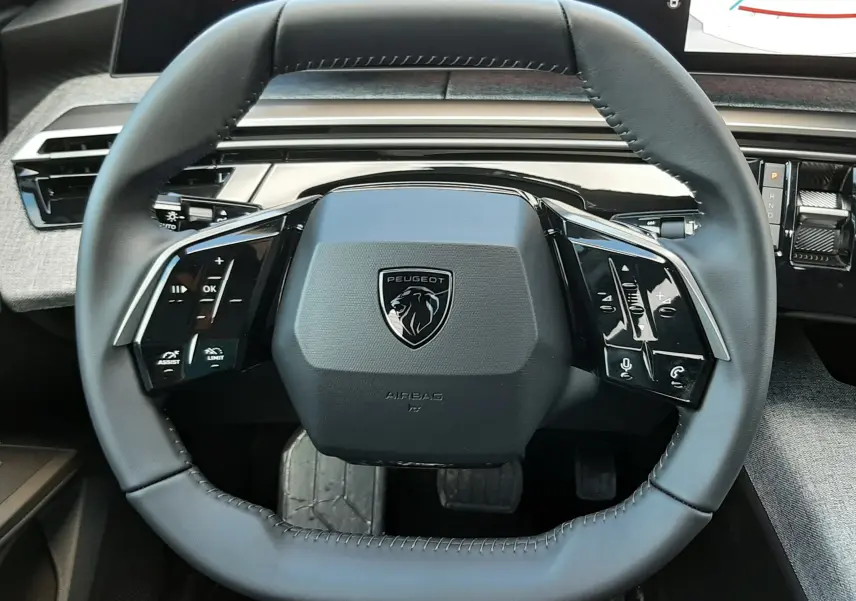 Gros plan sur le volant carré du Peugeot 5008 2025, avec commandes tactiles et tableau de bord numérique visible.