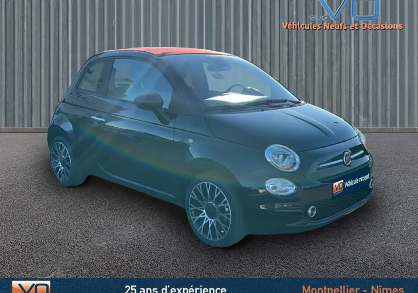 Fiat 500C noire vue 3/4 avant droit avec toit rouge et jantes alliage, stationnée devant un mur métallique.