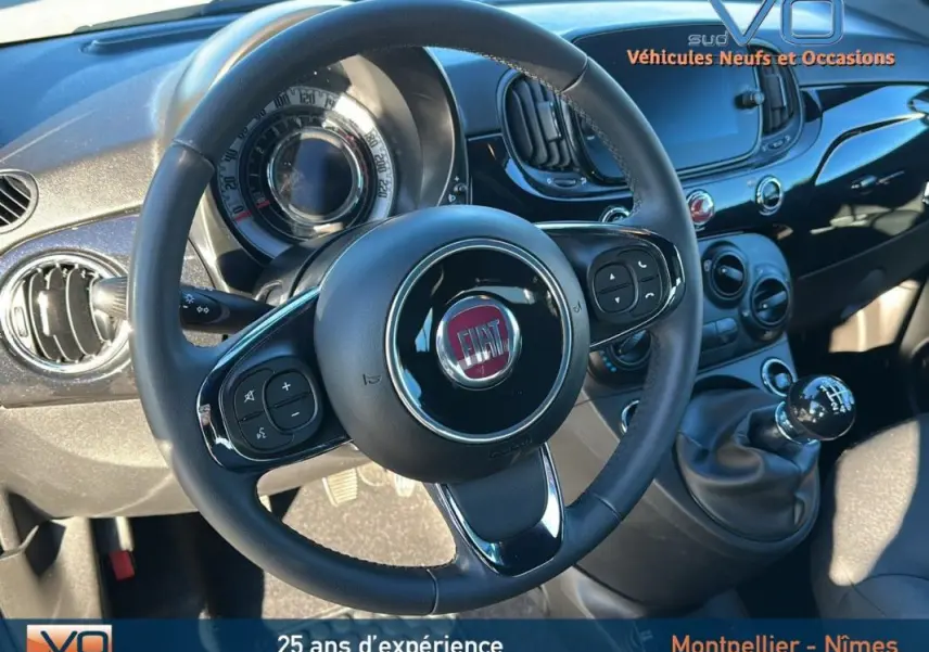Vue rapprochée de l'intérieur du Fiat 500C 2024 noir, mettant en valeur le volant, le tableau de bord et la boîte manuelle.