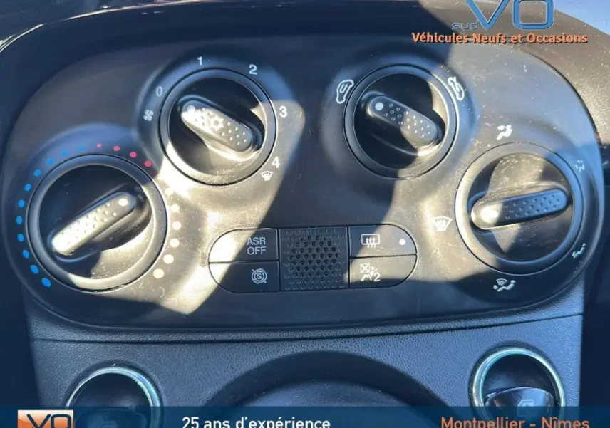 Gros plan sur les commandes de climatisation de la FIAT 500C noire 2024, version hybride avec options visibles.